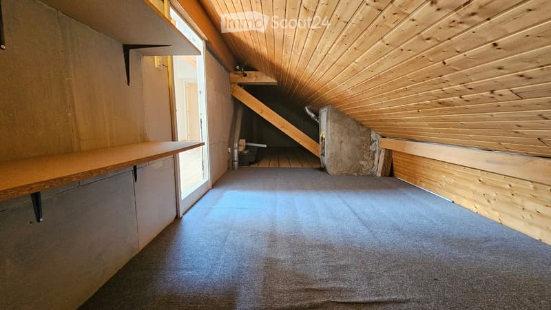 Empty attic space with wooden slanted ceilings, carpeted floor, and built-in wooden bench along one wall. Stairs lead down to another area.