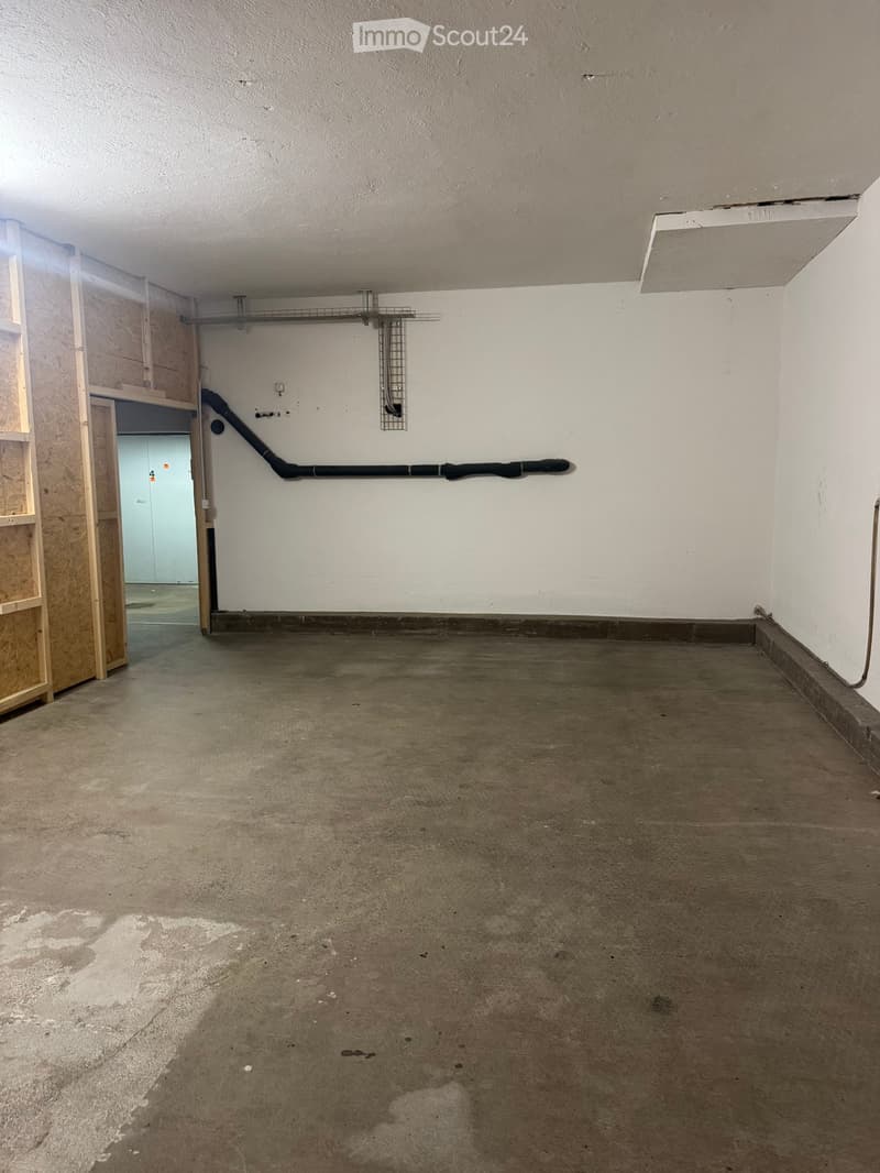 Empty room with concrete floor, white walls, and a metal shelf on the wall. There is a doorway leading to another room.
