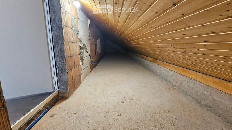 Empty hallway with wooden ceiling, concrete floor, and exposed brick wall on one side.