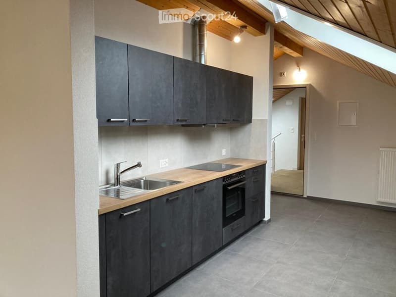 Modern kitchen with grey cabinets, wooden countertop, stainless steel sink and faucet, built-in oven, and exposed wooden beams on the ceiling.