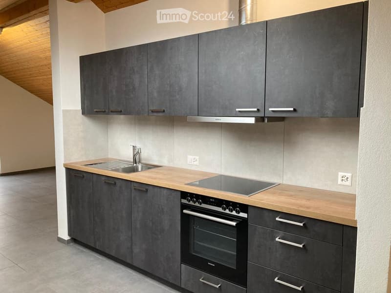 Modern kitchen with grey cabinets, wooden countertops, stainless steel sink, stove, and oven.