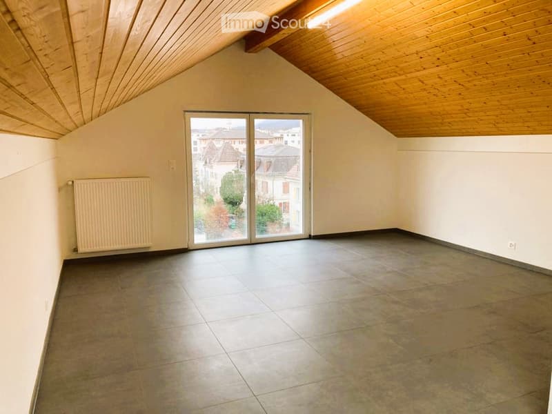 Empty room with wooden slanted ceiling, large glass sliding doors, tiled floor, radiator, and view of cityscape.