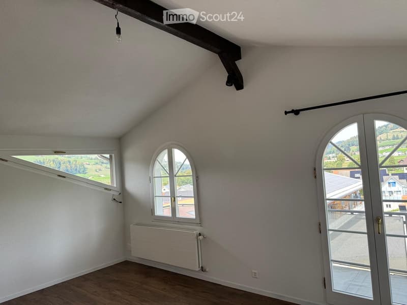 Empty room with wooden flooring, white walls, large windows, and a radiator. No furniture or equipment present.