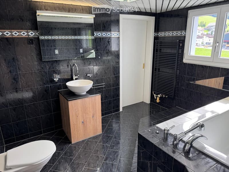 Modern bathroom with black marble tiles, a white sink, a bathtub, a toilet, and a large mirror above the sink.