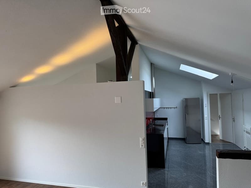Open-plan living and kitchen area with modern appliances, grey flooring, and white walls.