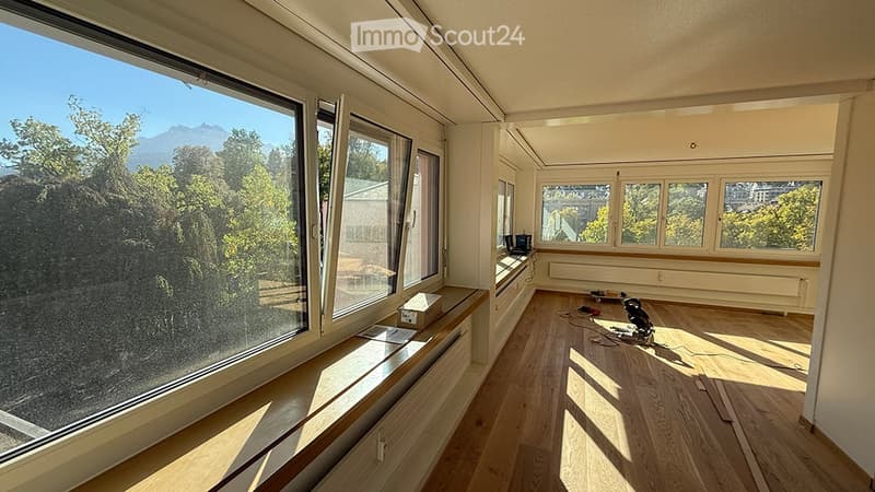 Bright, empty room with large windows offering a scenic mountain view, wooden flooring, and built-in bench seating along one wall.