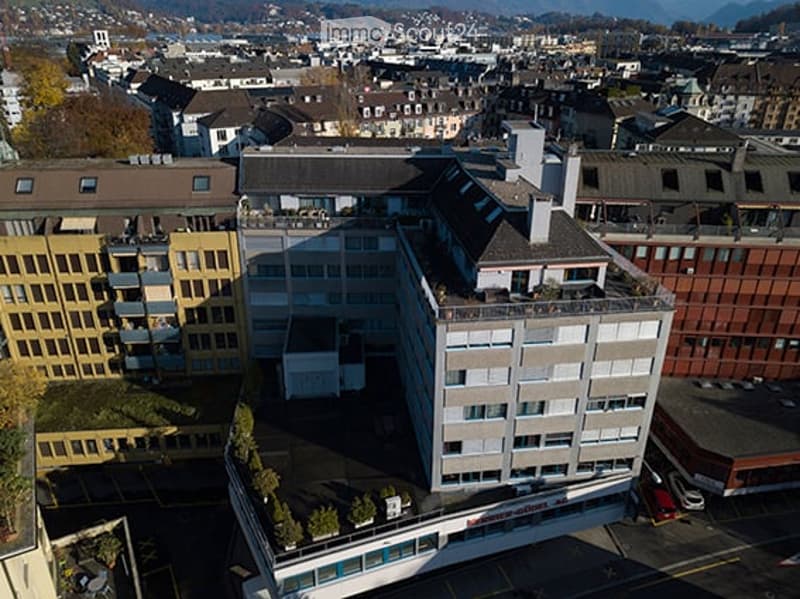 Aerial view of a multi-story building with a flat roof and surrounding structures in an urban setting.