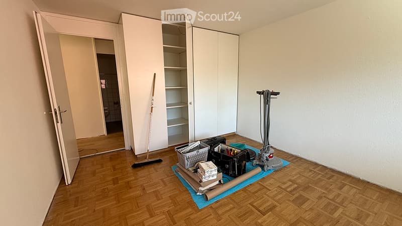 Empty room with wooden flooring, white walls, and a large open closet. Cleaning supplies and tools are placed on the floor.