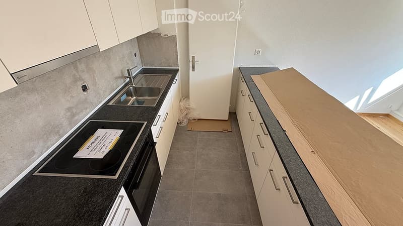 Empty kitchen with white cabinets, stainless steel sink, and black countertop. No appliances or furniture present.