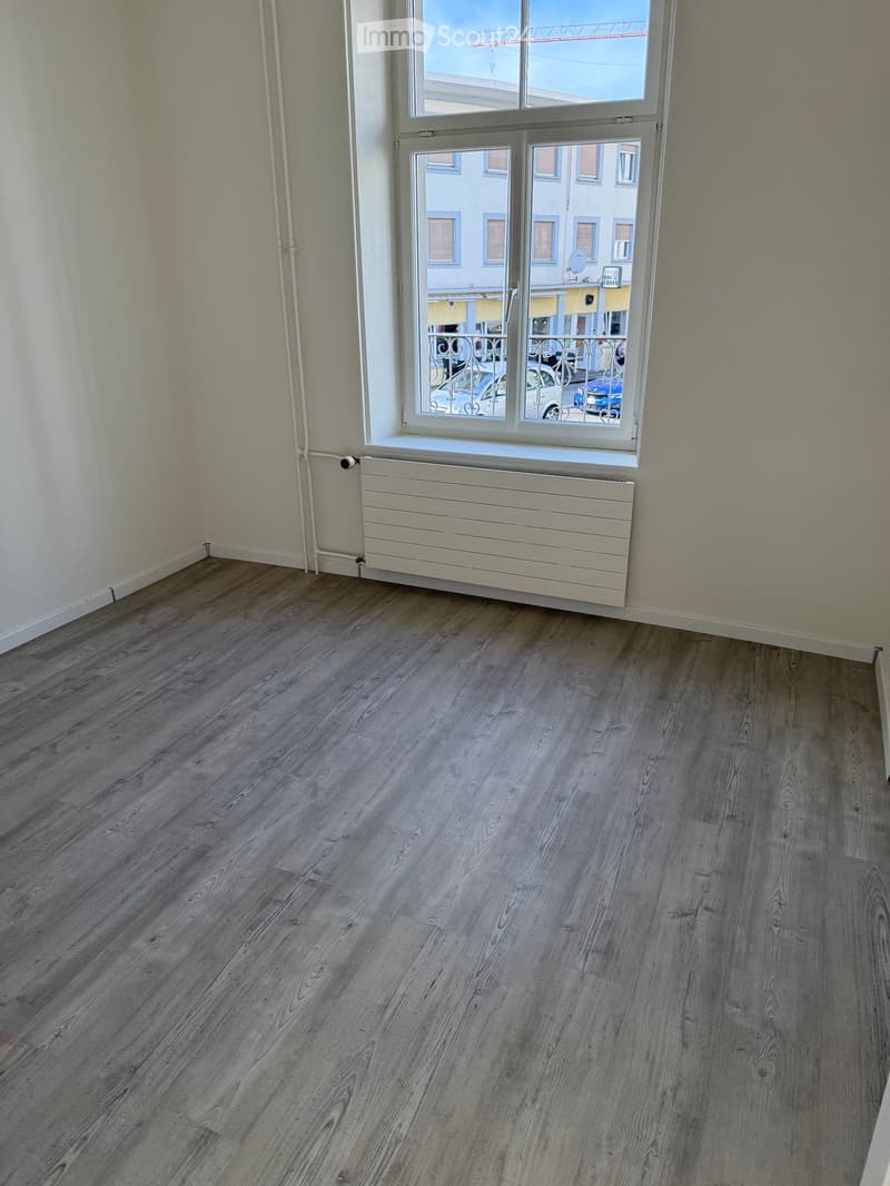 Empty room with wooden flooring, white walls, and a large window with a radiator below it.