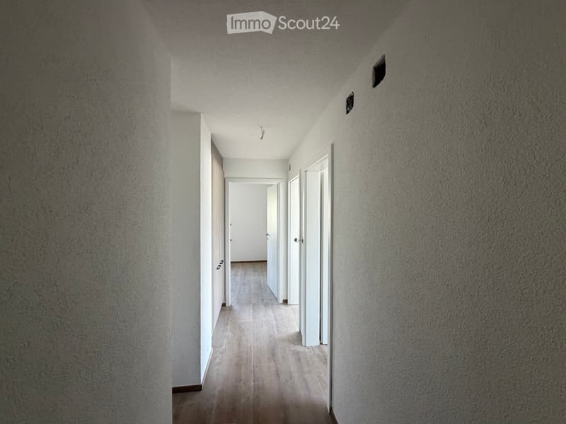 Empty hallway with beige tiled floor, white walls, and several doors leading to other rooms.