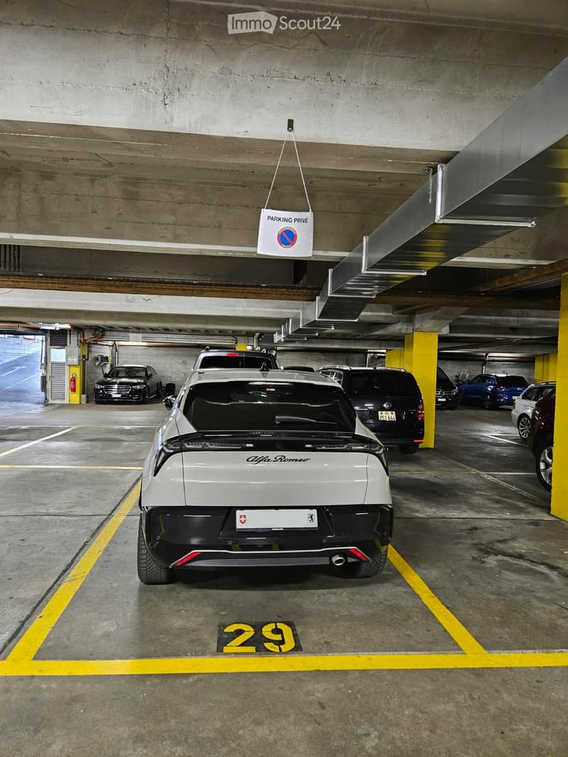 Underground parking lot with several cars parked in designated spots, marked with yellow lines and numbers, and a "Parking Privé" sign hanging from the ceiling.