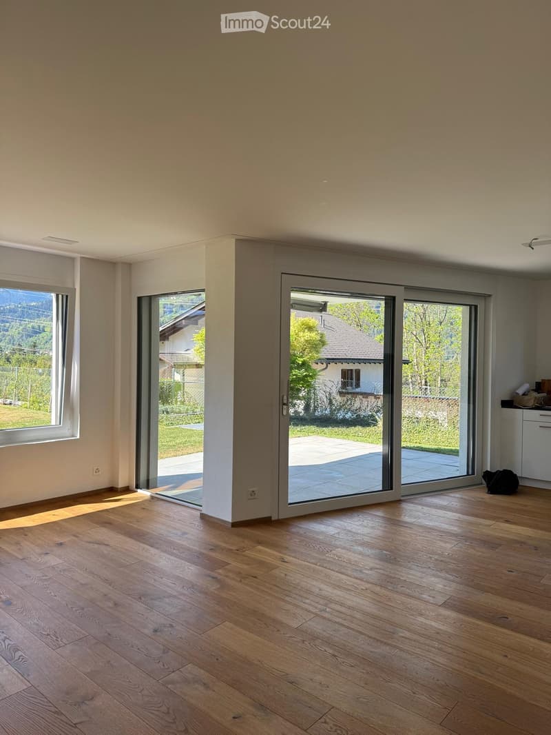 Empty room with wooden flooring, large windows, and sliding glass doors leading to a patio.