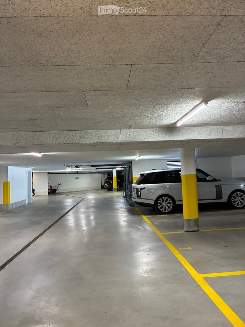 Underground parking area with concrete floors and walls, marked parking spaces, and a parked car.