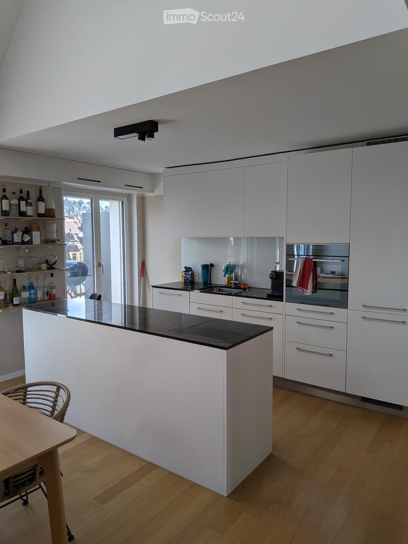 Modern kitchen with white cabinets, black countertops, and a central island. Includes a wooden dining table, chairs, and various appliances.