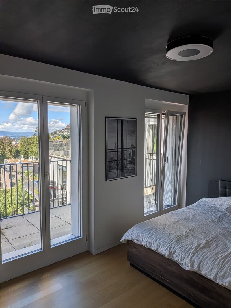 Modern bedroom with wooden floor, large windows, bed, and a mirror on the wall.