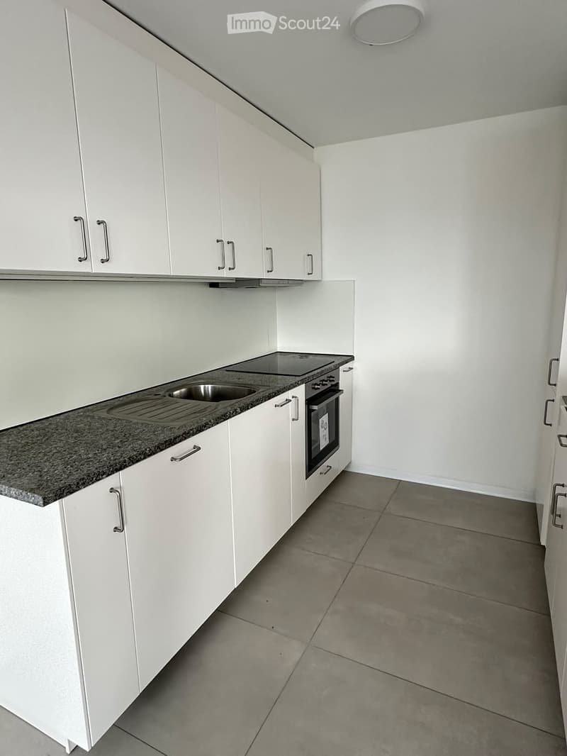 Empty kitchen with white cabinets, granite countertop, sink, and built-in oven. No appliances or furniture present.