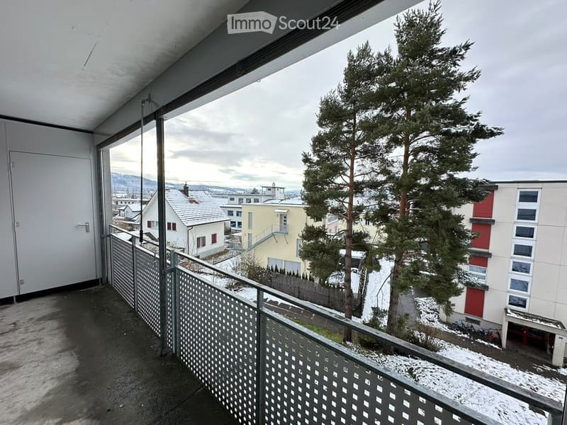 Balcony with metal railing, overlooking a snowy landscape with trees and neighboring buildings.