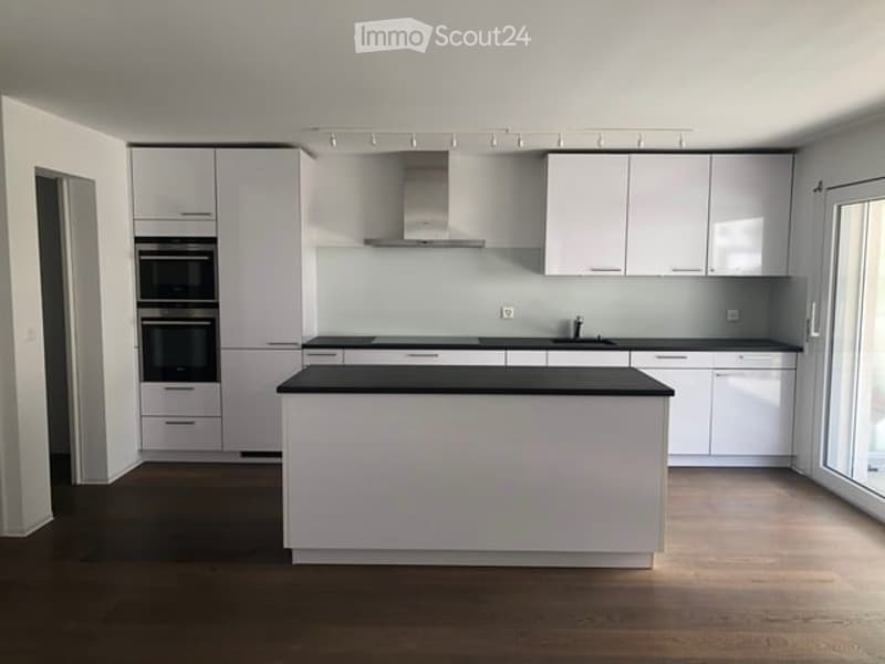 Modern kitchen with white cabinets, black countertops, and a central island. Features include built-in ovens, a sink, and ample storage space.