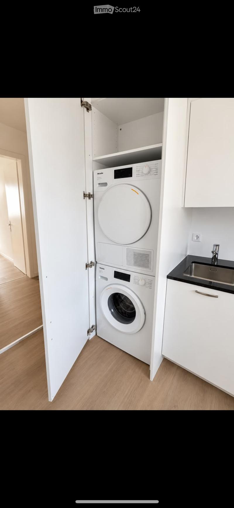 Compact bathroom with a white washing machine and dryer unit, a small sink, and white cabinets.