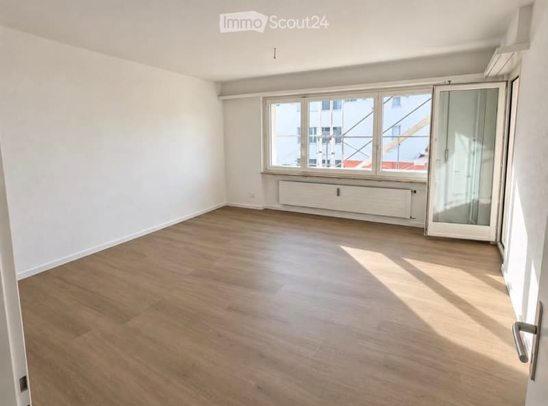 Empty room with wooden flooring, white walls, large windows, and a radiator. No furniture or equipment present.