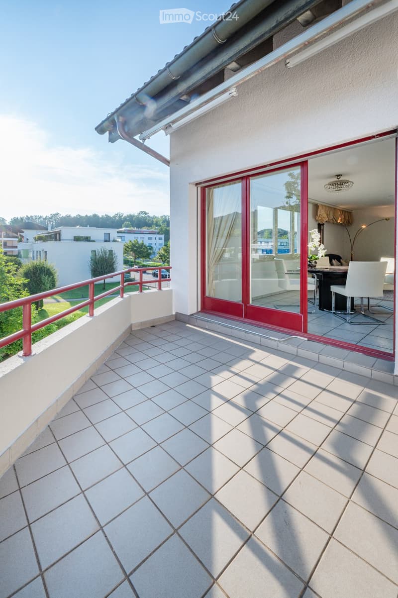 Balcony with tiled floor, red railing, and sliding glass doors leading to an interior space.