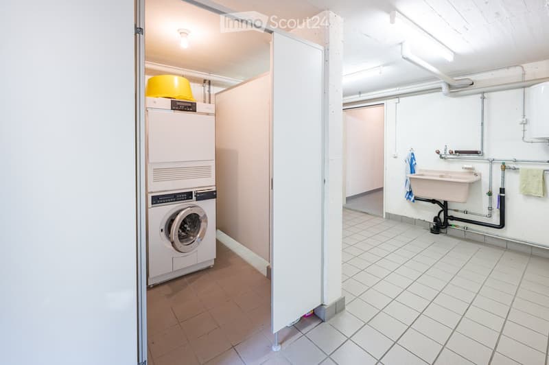 Clean, tiled bathroom with a private washing machine, a sink, and a towel hanging on the wall.
