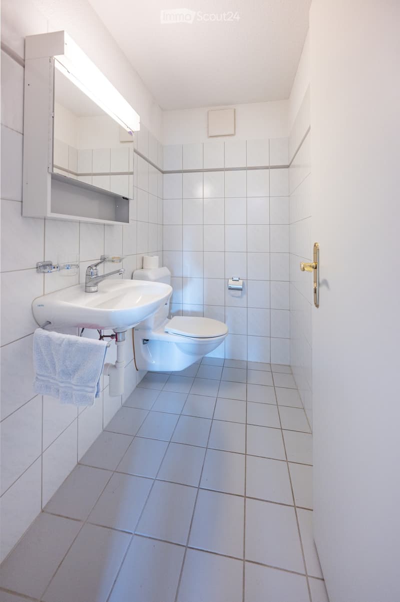 Modern bathroom with white tiles, a sink, toilet, towel, and a mirrored cabinet.