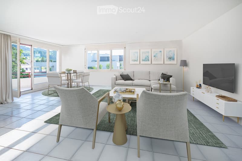 Bright living room with white walls, tiled floor, large windows, and a balcony. Features a grey sofa, coffee table, chairs, dining table, TV, and decorative items.