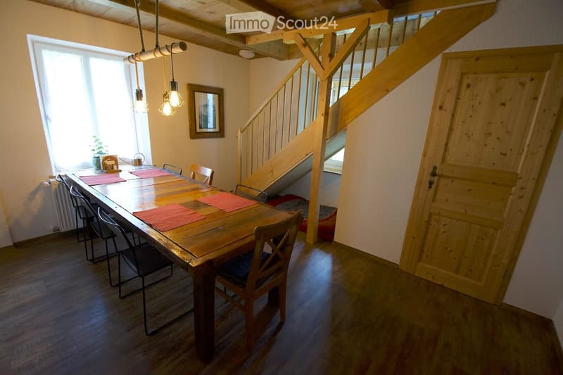 Bright dining area with wooden table, chairs, and a staircase leading to an upper level.