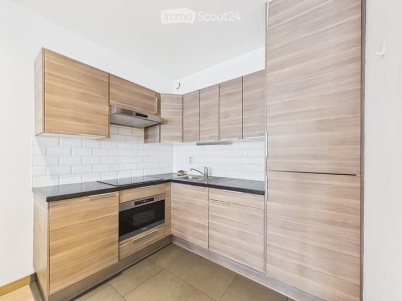 Modern kitchen with light wood cabinets, white tiled backsplash, stainless steel appliances, and a black countertop.