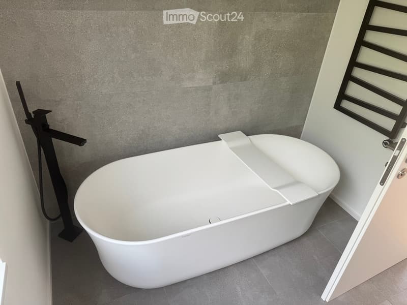 Modern bathroom with a sleek white bathtub, black faucet, and textured grey wall.