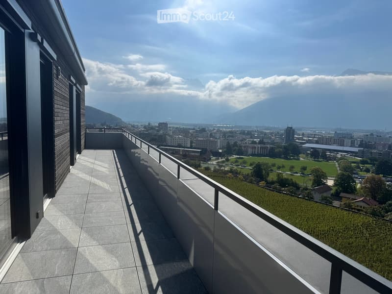 Modern balcony with tiled floor, glass railing, and expansive cityscape view including mountains and vineyards.