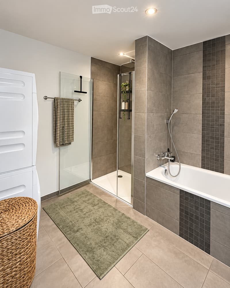 Modern bathroom with a bathtub, glass-enclosed shower, towel rack, wicker basket, and a green bath mat.