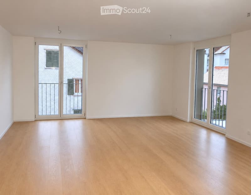 Empty room with light wooden flooring, white walls, and large sliding glass doors leading to a balcony.