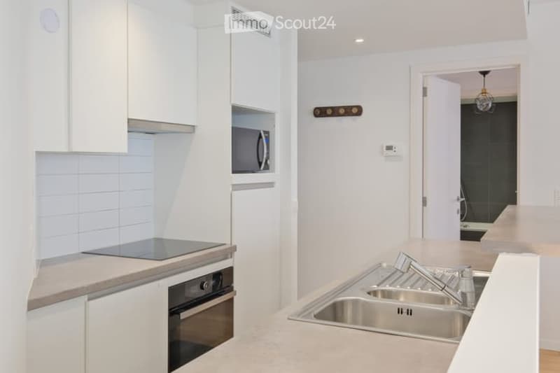 Modern kitchen with white cabinets, stainless steel sink, oven, microwave, and a sleek countertop.