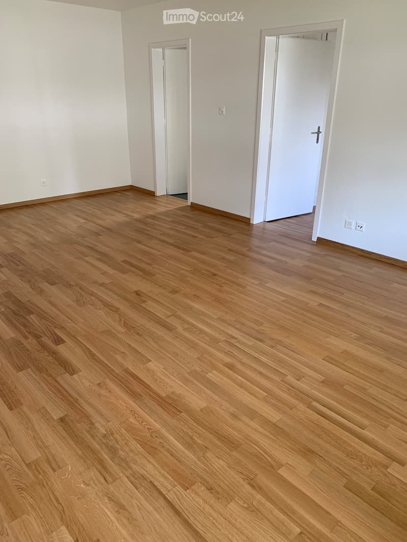 Empty room with light wooden flooring and white walls, featuring two white doors and electrical outlets.