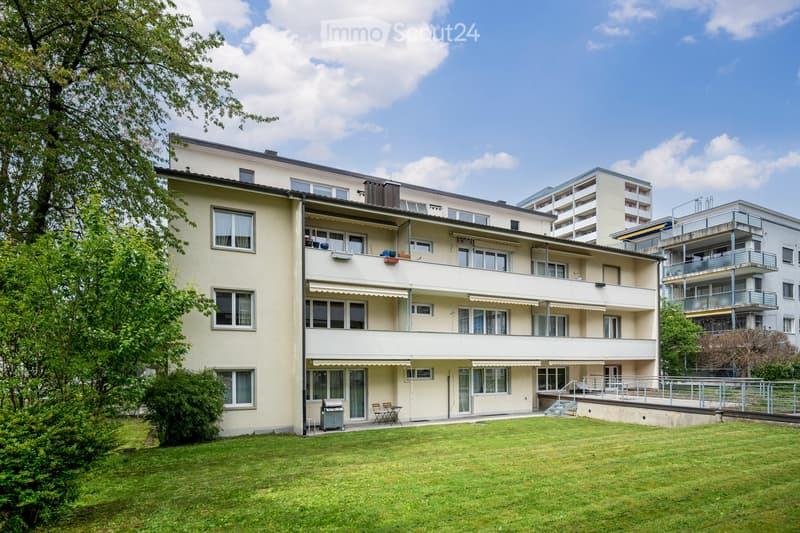 A multi-story residential building with balconies, large windows, and a well-maintained lawn in front.