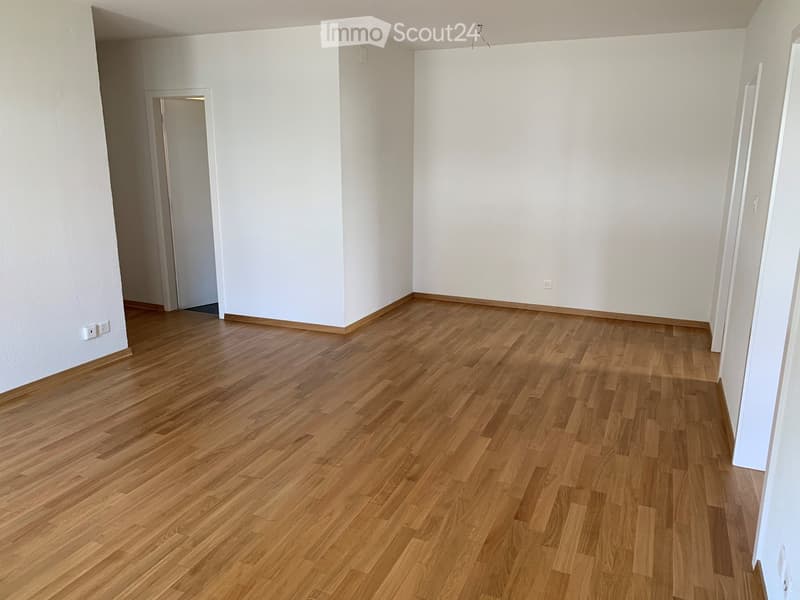 Empty room with light wooden flooring and white walls, featuring a doorway leading to another space.
