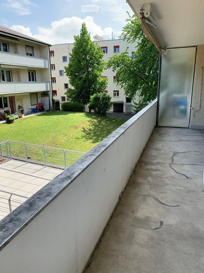 Balcony overlooking a grassy courtyard with trees and surrounding apartment buildings.