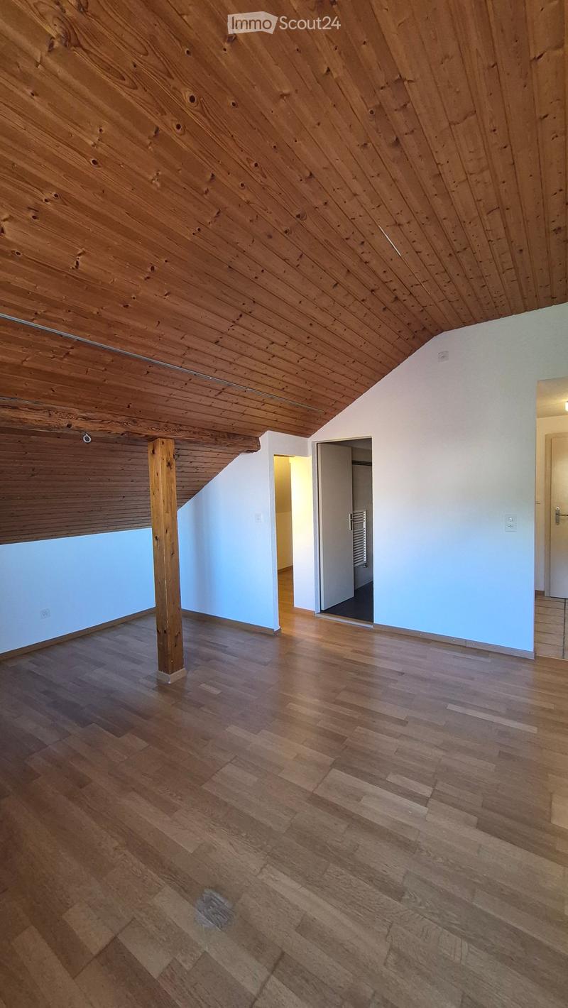 Empty attic space with wooden slat ceiling, exposed wooden beam, and wooden flooring. No furniture or equipment present.
