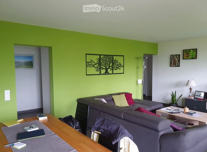 Modern living room with a grey sectional sofa, wooden coffee table, side table, floor lamp, potted plant, and artwork on the walls.
