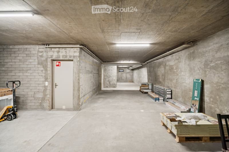 Underground corridor with concrete walls and ceiling, storage boxes, and a forklift visible.