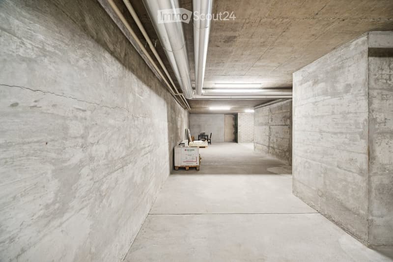 Concrete-walled room with a small table, chairs, and a storage unit, featuring exposed pipes and a clean, minimalist design.