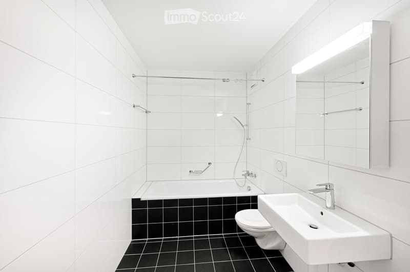 Modern bathroom with white tiled walls, black tiled floor, bathtub, toilet, sink, and mirror.