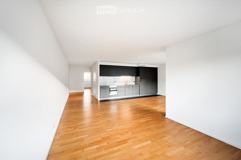 Open-plan space with light wooden flooring, white walls, and a fitted kitchen area featuring grey cabinets, a sink, and an oven.