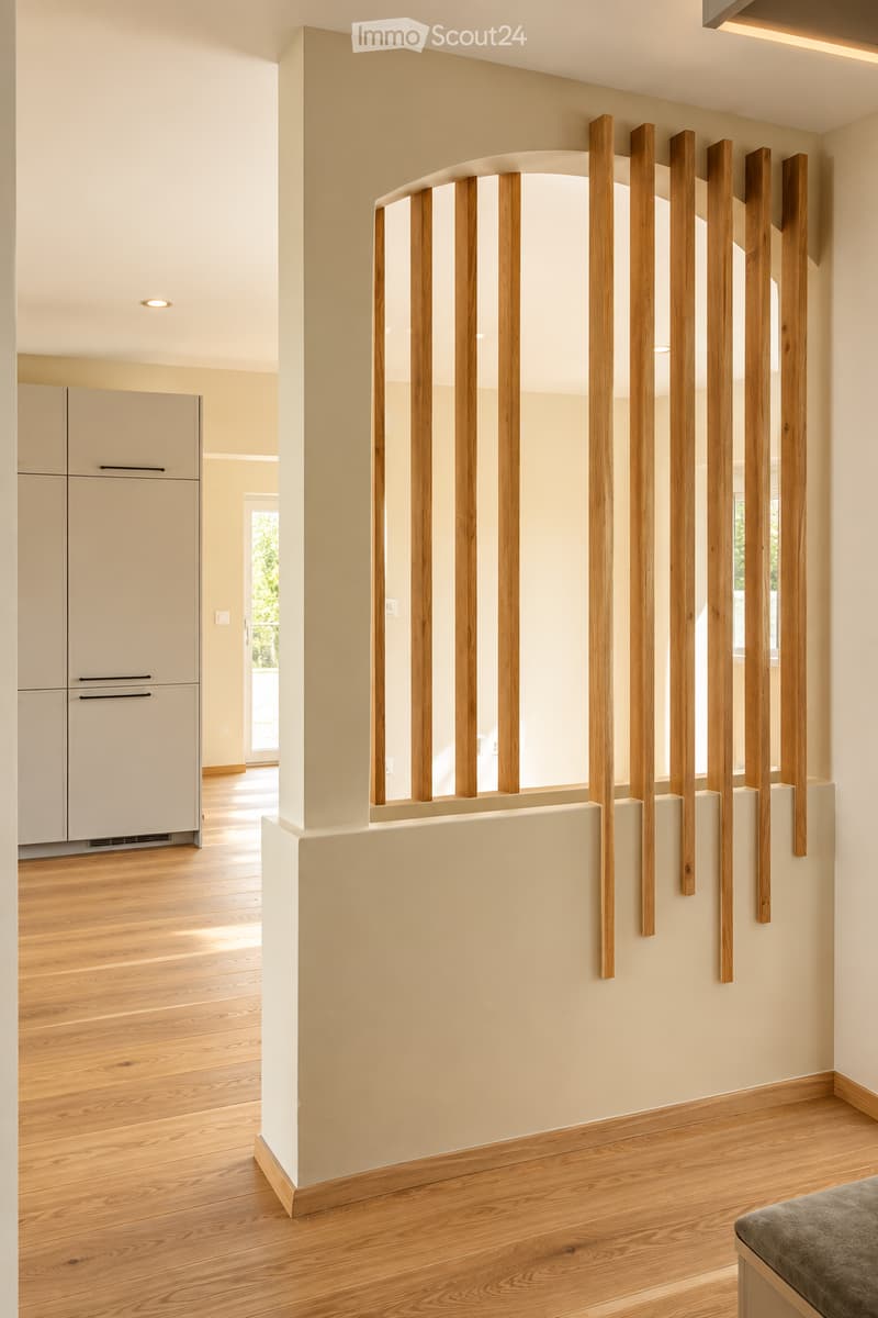 Modern hallway with light wooden flooring, white walls, and a decorative wooden partition with vertical slats. A grey cabinet is visible in the background, and a grey cushioned bench is partially visible in the foreground.