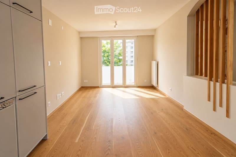 Empty room with light wooden flooring, white walls, and large glass doors leading to a balcony. No furniture or appliances are present.