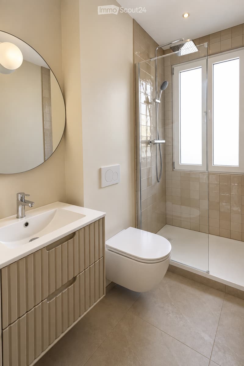 Modern bathroom with a sleek sink, mirror, toilet, and glass-enclosed shower with multiple showerheads.