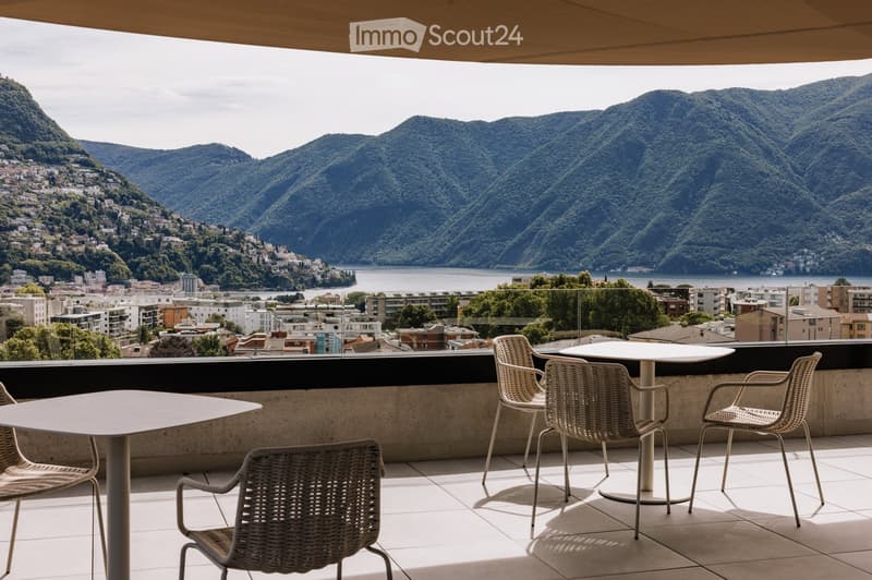 Balcony with a scenic mountain and lake view, featuring a white table and four wicker chairs.